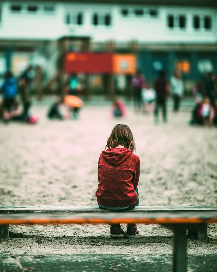 Ein Kind sitzt auf einer Bank am Spielplatz.
